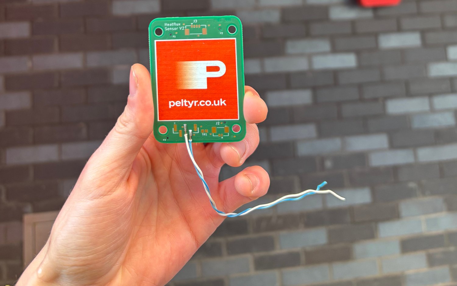 Peltyr printed heat flux sensor board held in a hand, with its two signal leads